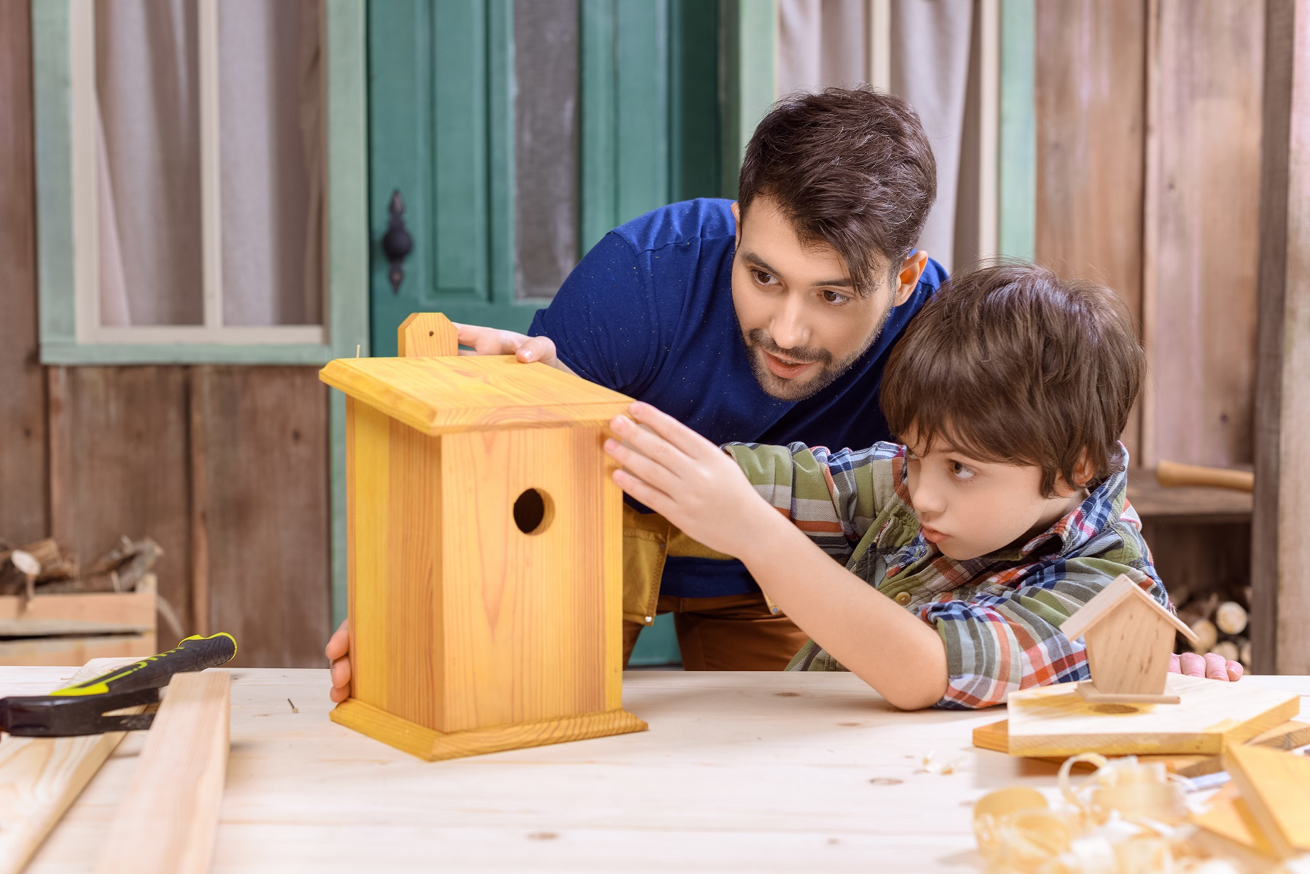 Concentrated father and son making wooden birdhouse together in workshop